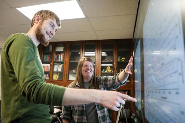 Man and a woman looking at graphs displayed on a smartboard